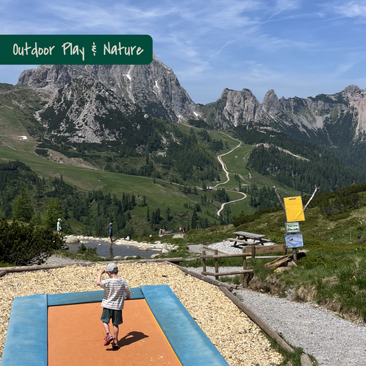 Child jumping on trampoline on the Aqua Trail with view on mountains in Carinthia, Austria. Picture of KidsTravelAdventures.